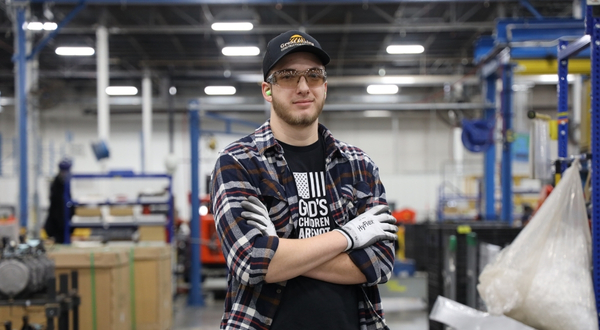 A K-State Salina student stands smiling inside the Great Plans Manufacturing Plant as he works part time for the company through a scholarship program offered by the campus. 