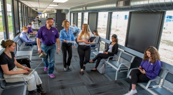 Two K-State Salina students in professional attire walk through a busy airport as they talk with an aviation professional.