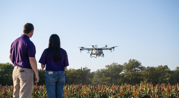 An instructor and K-State Salina student fly a large ag drone over a field.