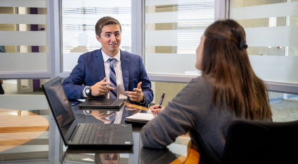 A student in a suit and tie speaks with an employer inside of a conference room.