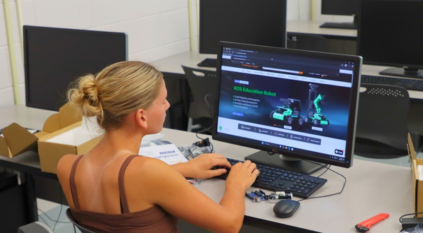 A youth camper watches an instruction video on a computer about building a robot with tools laid out next to her.