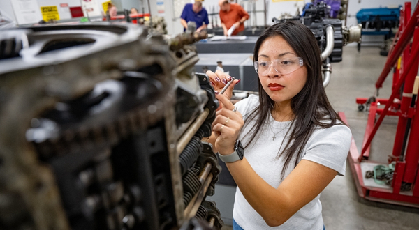 A K-State Salina student wearing protective glasses inside of an aircraft hangar inspects and works on a large aircraft engine.