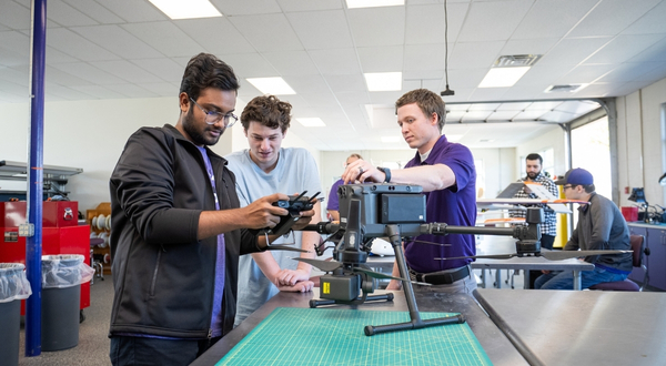 Two students look at a remote controller of a drone, while a K-State Salina faculty member instructs.