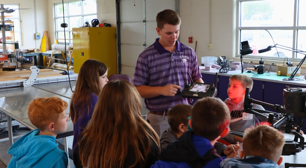 A UAS instructor at the K-State Salina campus holds a drone and remote while talking with children control during a youth camp.