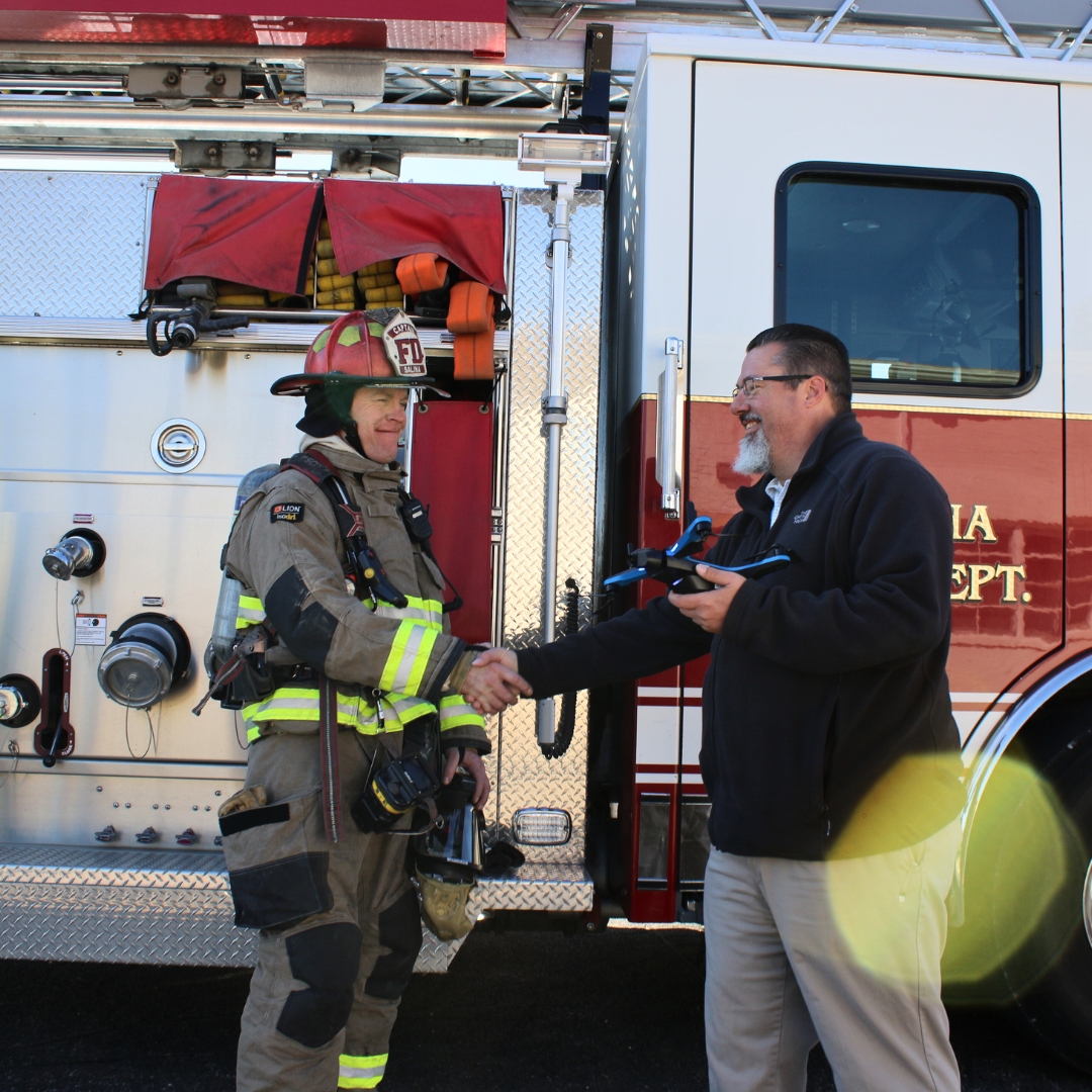A K-State Salina drone instructor holds a drone and shakes the hand of a firefighter