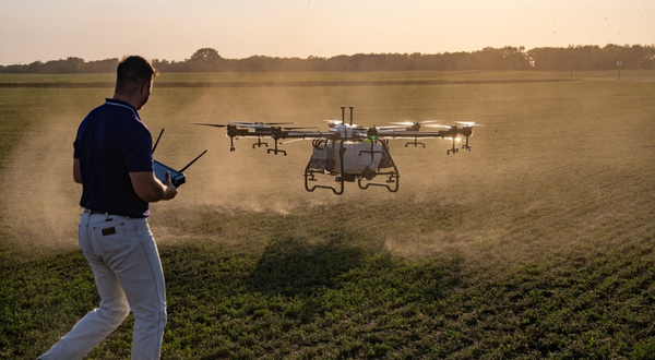 A drone operator lands a large drone in a field during sunset.