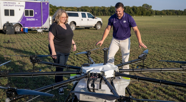 A UAS instructor inspects a large drone in the middle of a field.