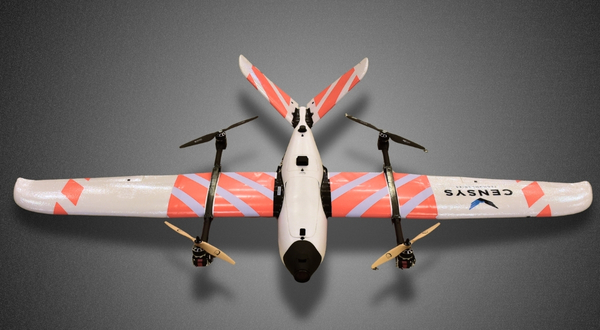 A Censys Sentaero 5 UAS that is offered at K-State Salina sits in a grass field at dusk with the grass below illuminated in red and green colors from the lights of the aircraft's sensors.
