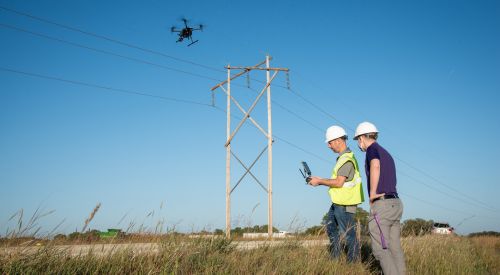 An instructor and learner look at a remote control while flying a drone near a power line as apart of K-State Salina's training for utilizing UAS for utility providers.