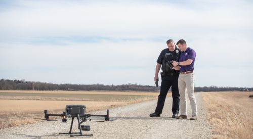 A police officer inspects the remote control to operate a drone in an open field with a K-State Salina UAS instructor. 